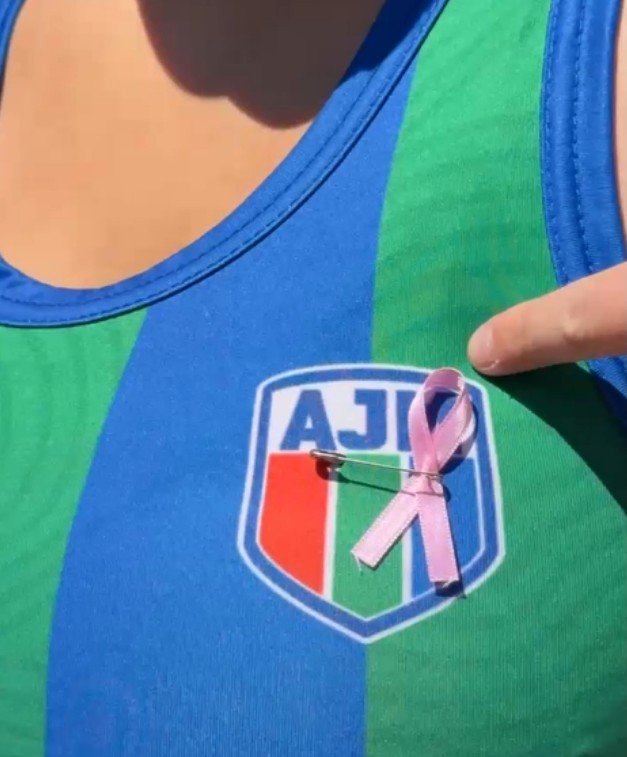 Detalle del escudo del Club Alianza Jesús María con un lazo rosa colocado en el pecho de una jugadora, símbolo de la campaña de concientización sobre el cáncer de mama.